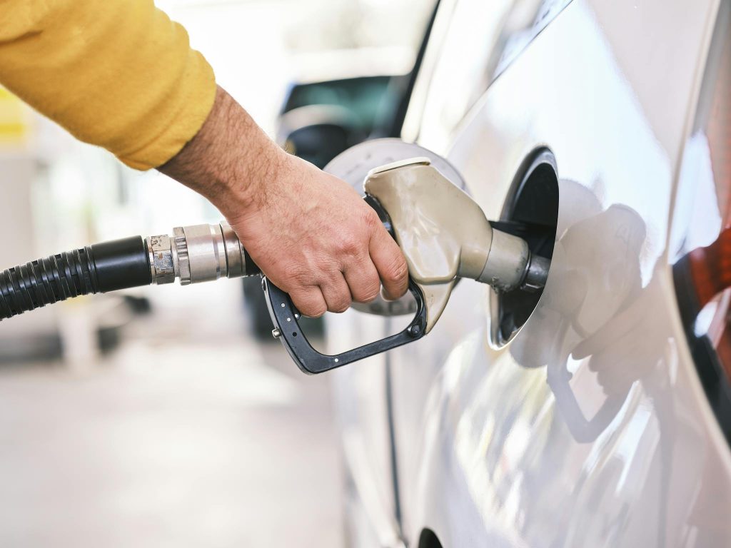 Close-up of a person refueling a car with a gas nozzle at a station.